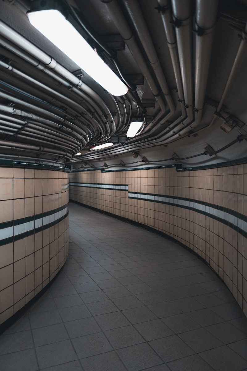 A curved, tiled hallway with overhead pipes.