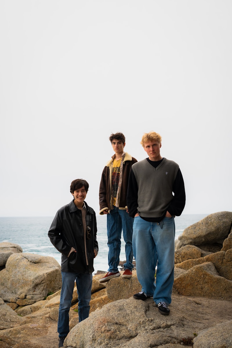 Three young men pose by the ocean.